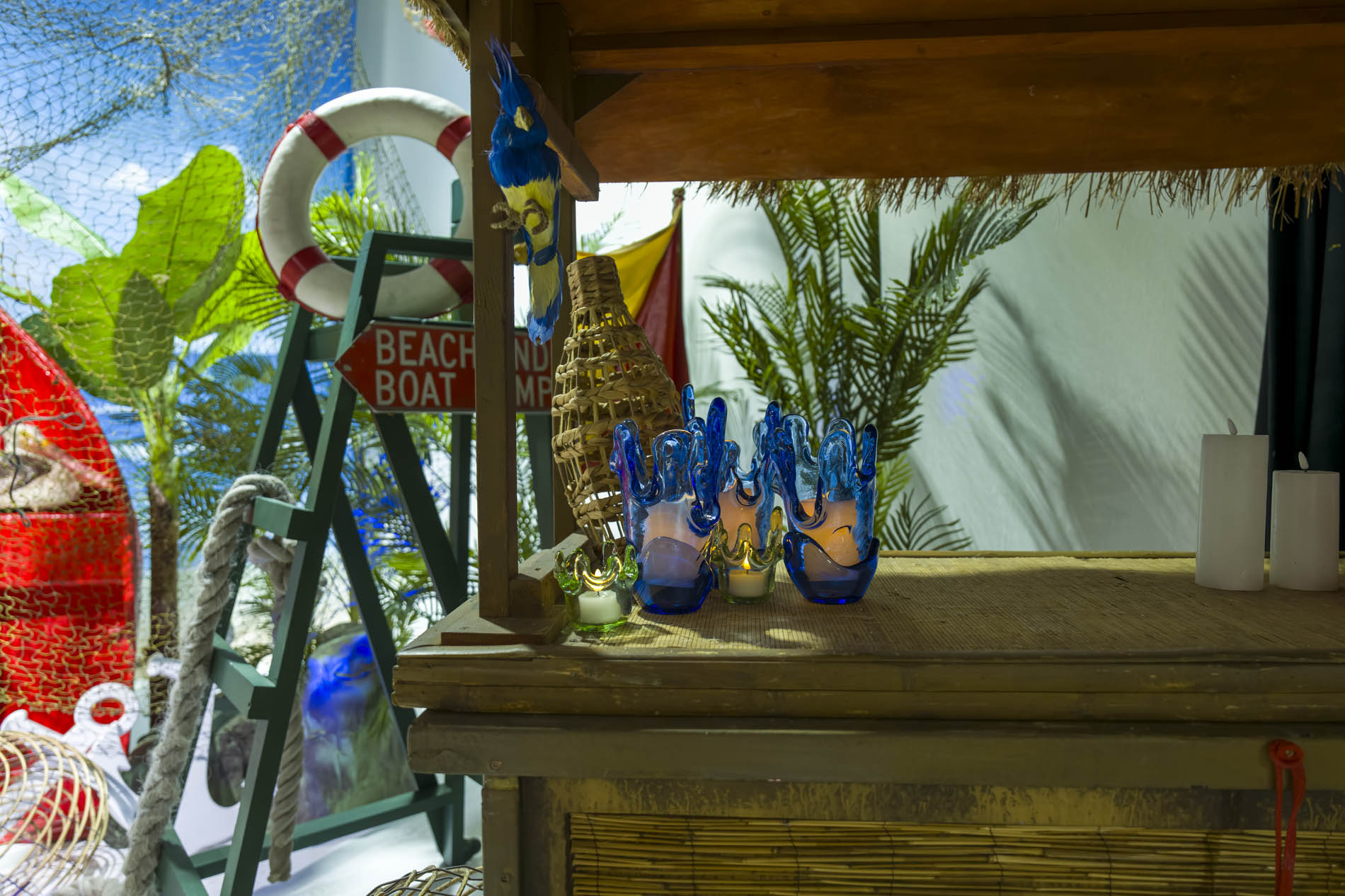 Timber bar top with candles and blue glass vessels beside a green lifeguard ladder and life ring