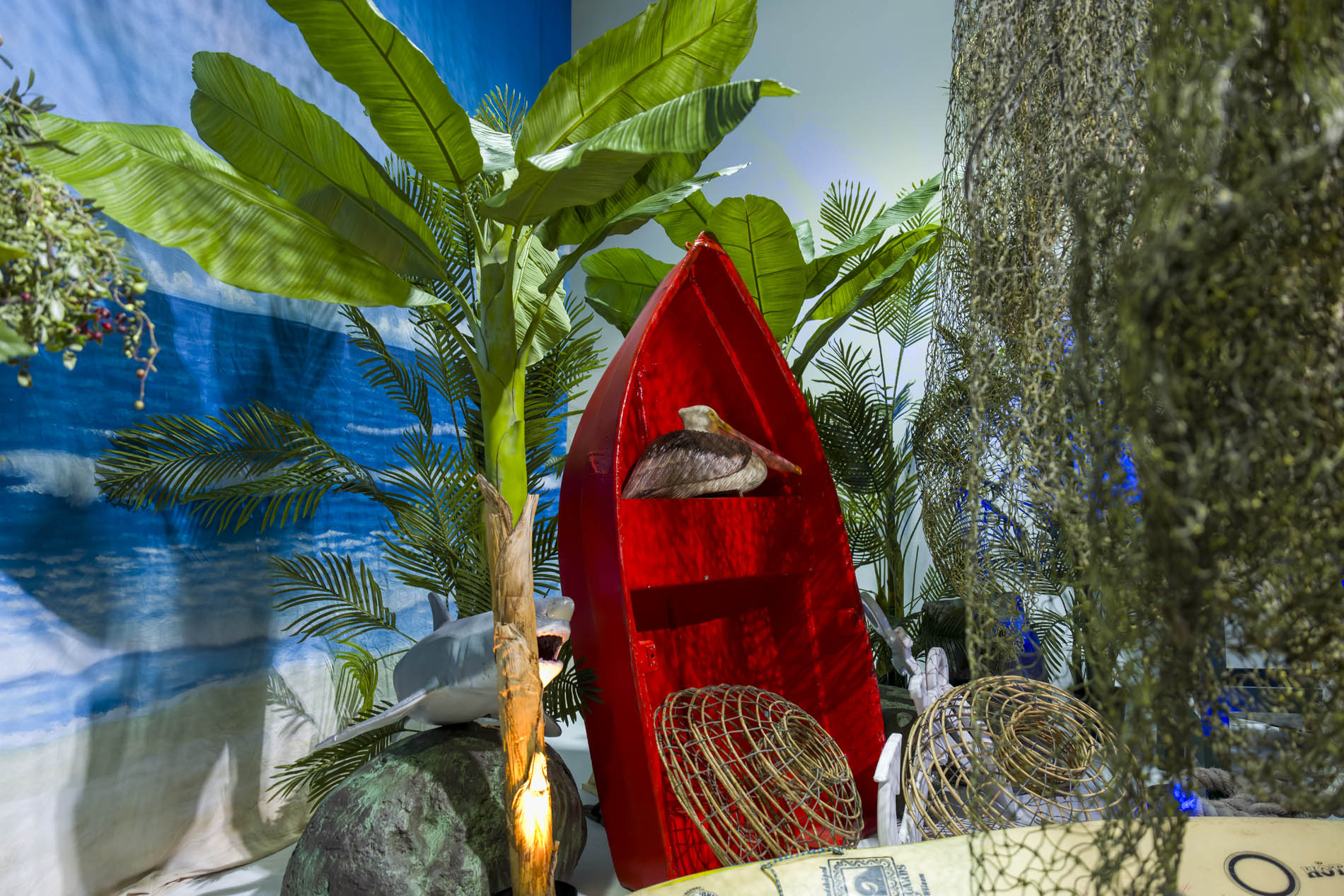 Red timber rowboat among banana palms with wicker lobster pots and a painted ocean backdrop